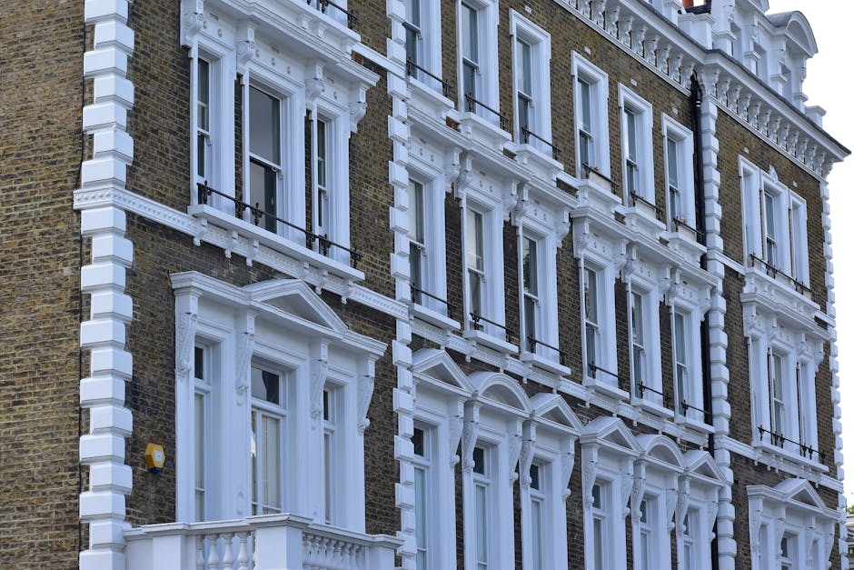 Photograph of a multi-storey Victorian-style house on Old Brompton Road, South Kensington, with ornate white decorative trim around the windows and balconies contrasting against the brown brick facade. The building features several large sash windows with black metal railings on small balconies, and the overall architecture showcases intricate detailing around the window frames and cornices. The image captures the exterior of the property during daylight, with natural light highlighting the texture of the brickwork and the white decorative elements. This setting is relevant to house removals and home relocation services, illustrating the type of residential property involved, and is suitable for a page discussing house removals in South Kensington, provided by South Kensington Removals, focused on packing, furniture transport, and loading processes involved in moving services.