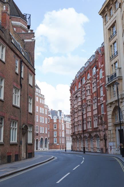Photograph of a multi-storey Victorian residential building with a red brick facade, decorative arch windows, and distinctive stone detailing characteristic of homes along Old Brompton Road in South Kensington. The building features several bay windows, small balconies with wrought iron railings on the lower floors, and a central entrance with a set of steps leading up to double doors. Above the entrance, there are arched window openings and several chimneys protrude from the roofline. The image is taken from the street, showing the building front and pavement below, with clear daylight and a blue sky in the background. This type of architecture is typical for area house removals and residential relocations, highlighting the importance of professional moving services like those offered by South Kensington Removals for home relocation and furniture transport in South Kensington.